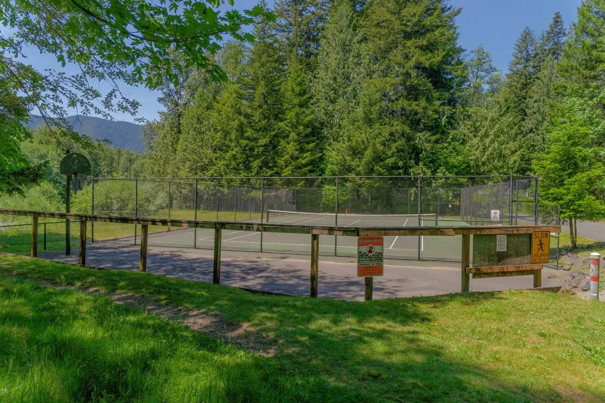 An exterior view showing a well-maintained tennis court and basketball hoop, bordered by tall trees. The scene invites active play and community engagement.