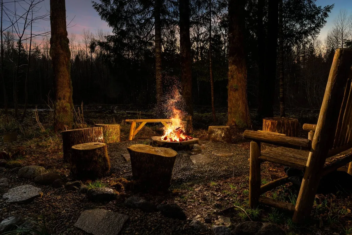 A cozy campfire surrounded by wooden seating, nestled among towering trees. The warm glow of the fire suggests evenings spent sharing stories and stargazing after a day of outdoor adventures.