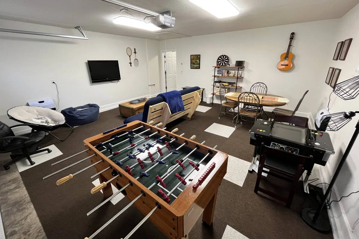 A playful, casual space highlighted by a prominent foosball table, a dining table for games or snacks, a projector screen for movies, and a guitar for musical moments. The room exudes a relaxed, fun atmosphere ideal for family entertainment.