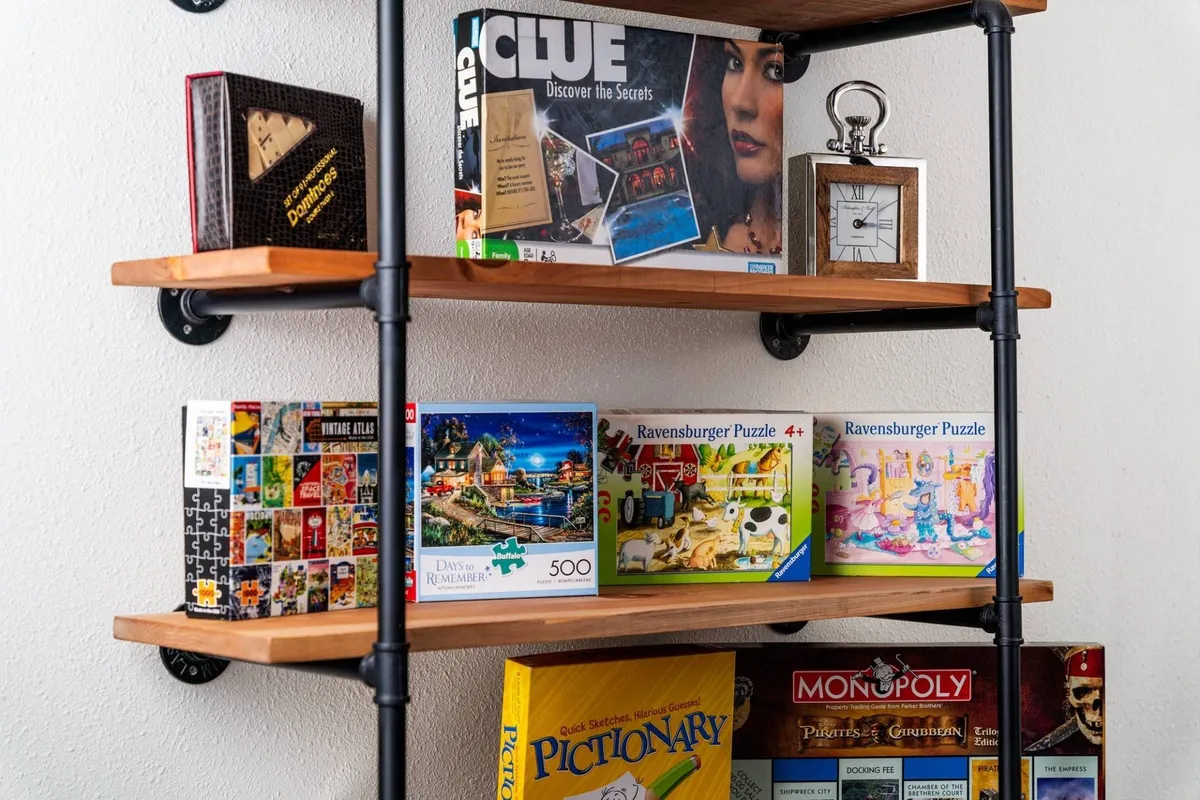 A nostalgic display of board games and puzzles arranged on a shelf, accompanied by a decorative clock. The setup evokes memories of family game nights and puzzle-solving marathons.