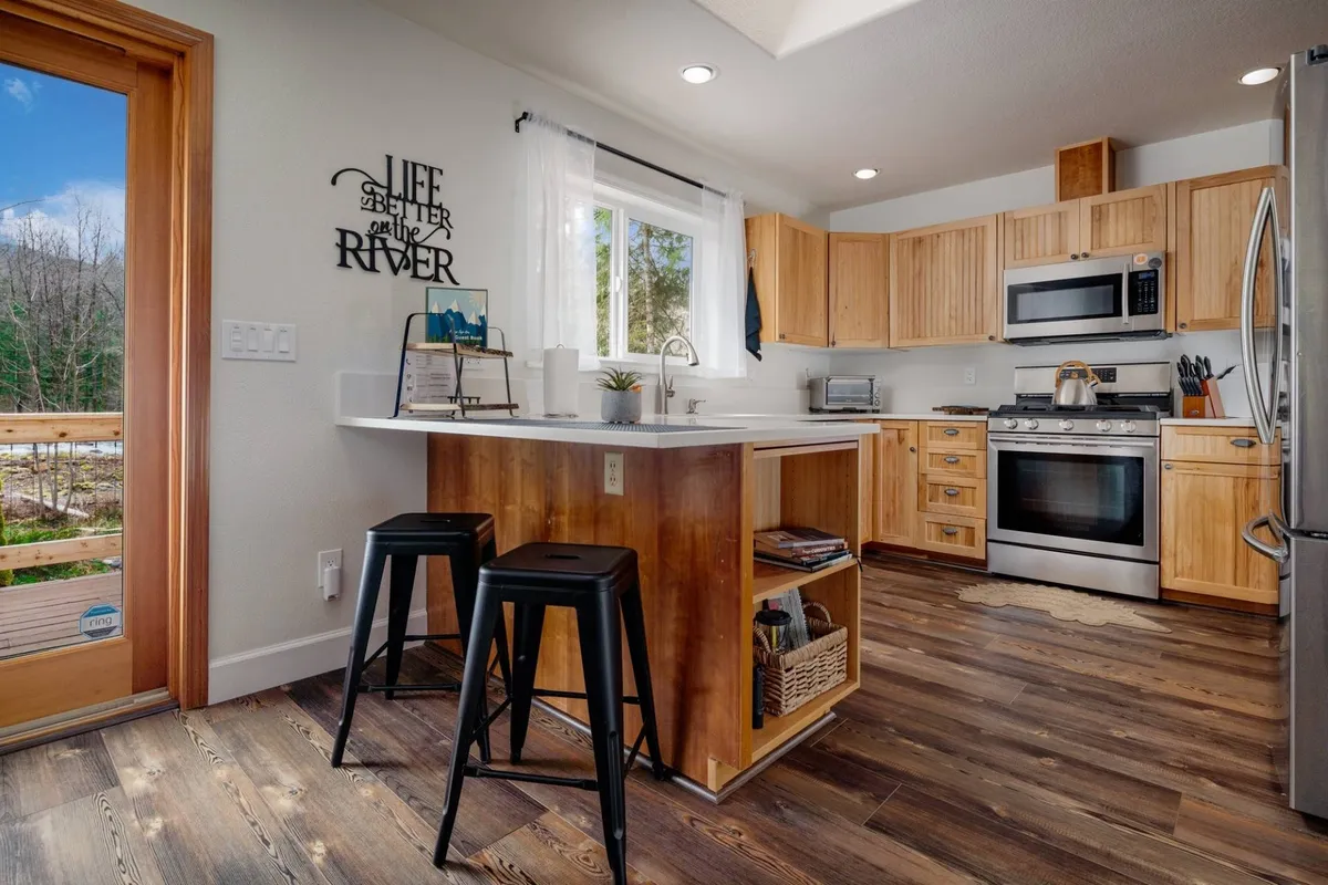 A beautiful, functional kitchen with a spacious island, wooden cabinetry, stainless steel appliances, and a large window offering serene views. Ideal for preparing meals together or entertaining guests, this kitchen is clearly upgraded and designed for togetherness.