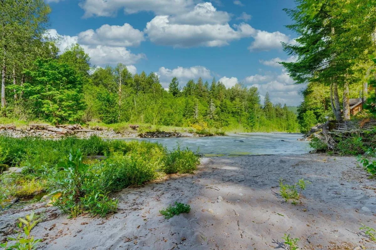 A tranquil riverbank scene with a sandy edge, bordered by trees and open sky. The natural setting offers a peaceful place for morning meditations, riverside walks, or stargazing at night.