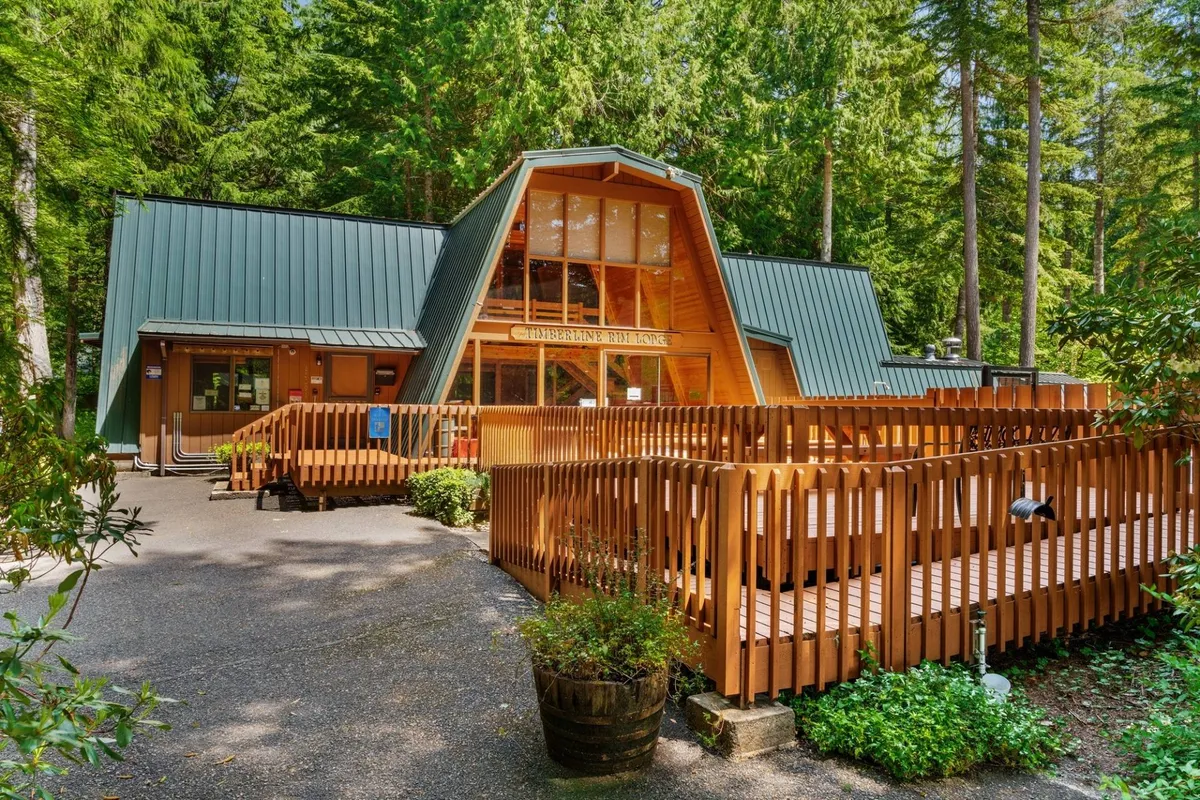 This exterior shot features an inviting A-frame structure with a spacious wooden deck surrounded by trees. The setting evokes a tranquil and welcoming atmosphere, ideal for relaxing with pets. The deck connects directly to the outdoors, suggesting a natural flow between the home and nature.