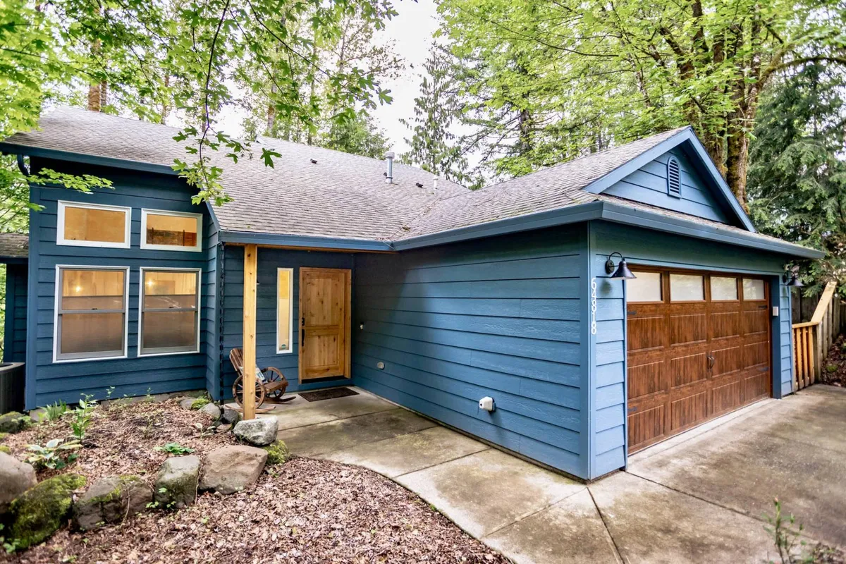An inviting view of the home's blue wooden exterior, featuring a welcoming wooden front door and garage door with windows, all set amongst lush greenery. The overall mood is homey and intimate, suggesting a peaceful retreat away from the bustle of daily life.
